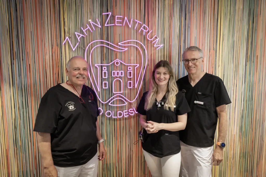 Behandlerteam des ZahnZentrums Bad Oldesloe vor der farbigen Wand mit Neon-Logo